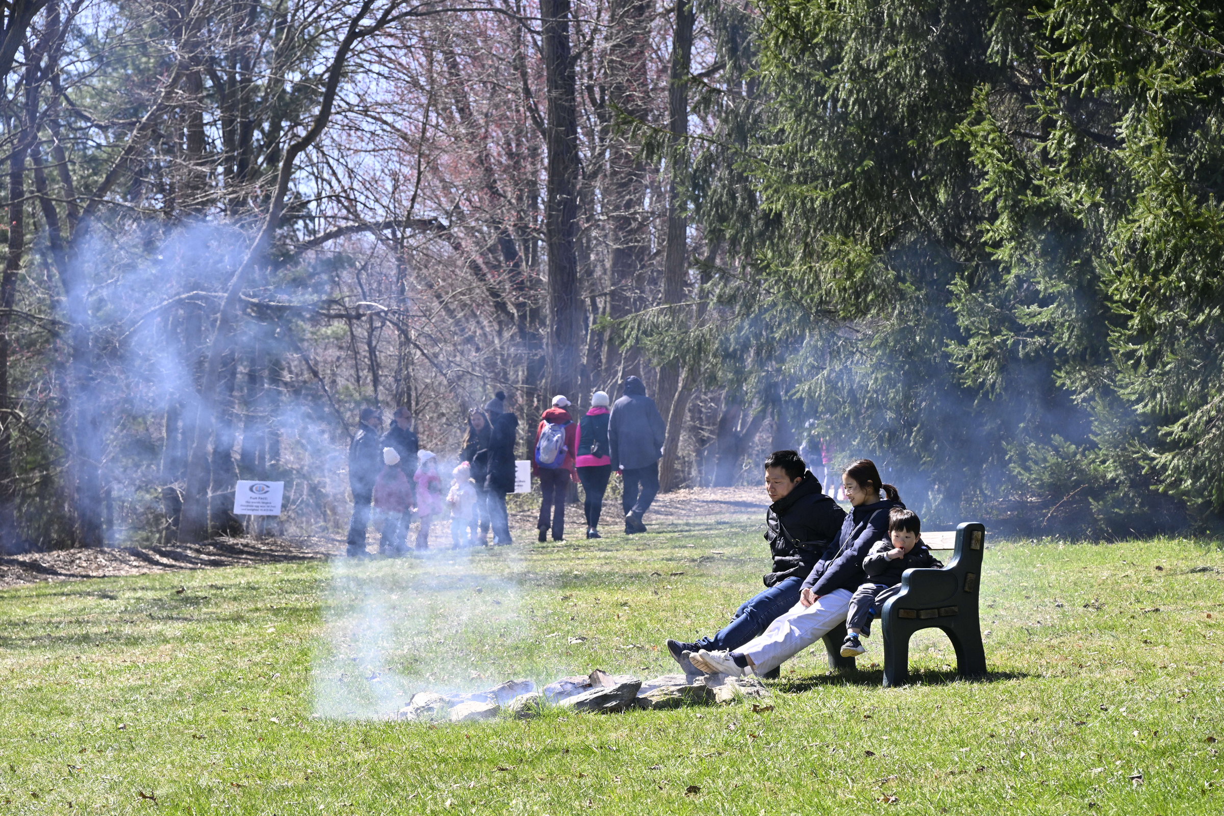A family warms themselves by a fire while others stroll down a path during the Coppermine Eggstravaganza at Cascade Park in Hampstead. (Thomas Walker/Freelance)