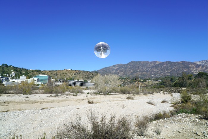 A Californian desert scape featuring some buildings and a lens-like object in the middle of the sky