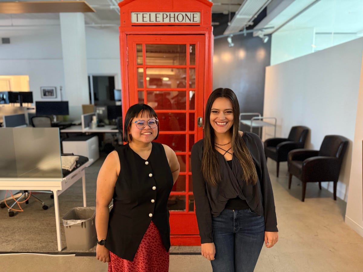 Two people stand by a red telephone booth