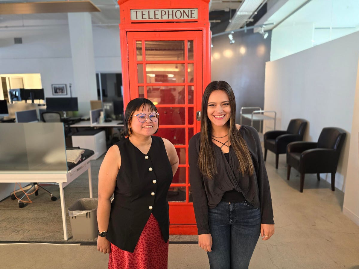 Two people stand by a red telephone booth