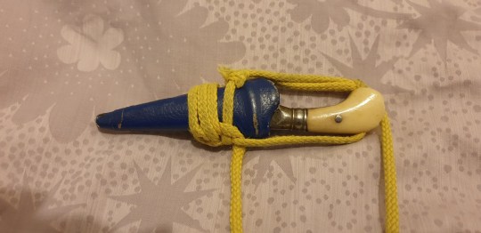 A photo of a kirpan - a very small dagger wrapped in a yellow rope, with a cream handle an din a navy sheath