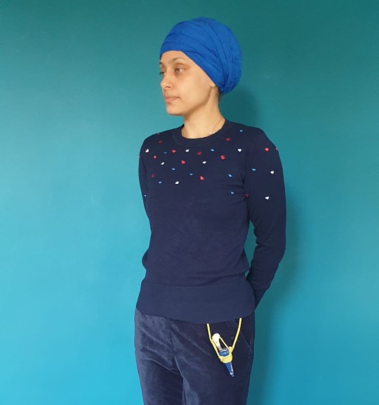 Karen wearing navy and a blue turban, standing in front of a blue wall - a kirpan is hanging from her trousers