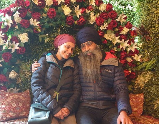 Karen sitting with her husband - both in turbans, with a floral display behind them