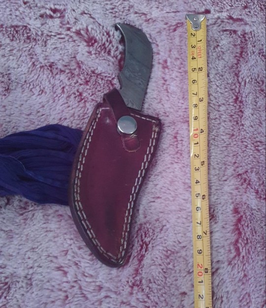 A kirpan in a brown sheath, next to measuring tape - it is just under 8 inches long