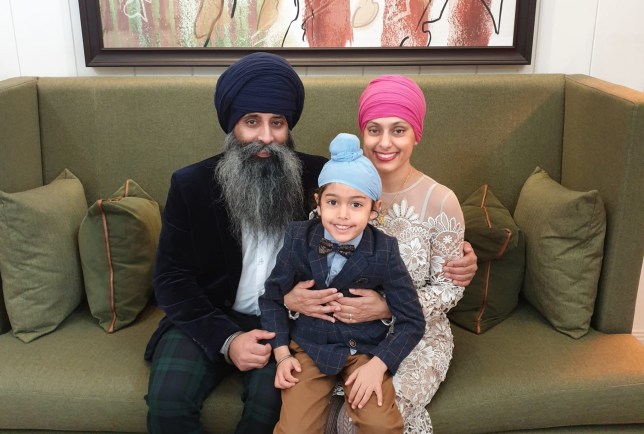 Karen sitting on a green sofa with her husband and their son on her lap - all three dressed up in suits, a dress and turbans.